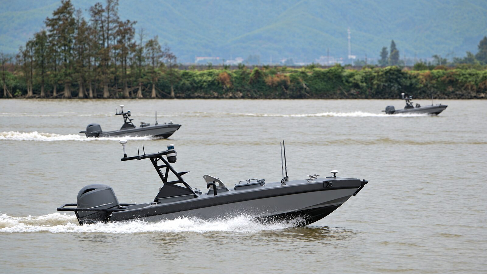 Three grey workboats underway on a river, each carrying a mast with antennas, a lidar and a camera, and an outboard engine